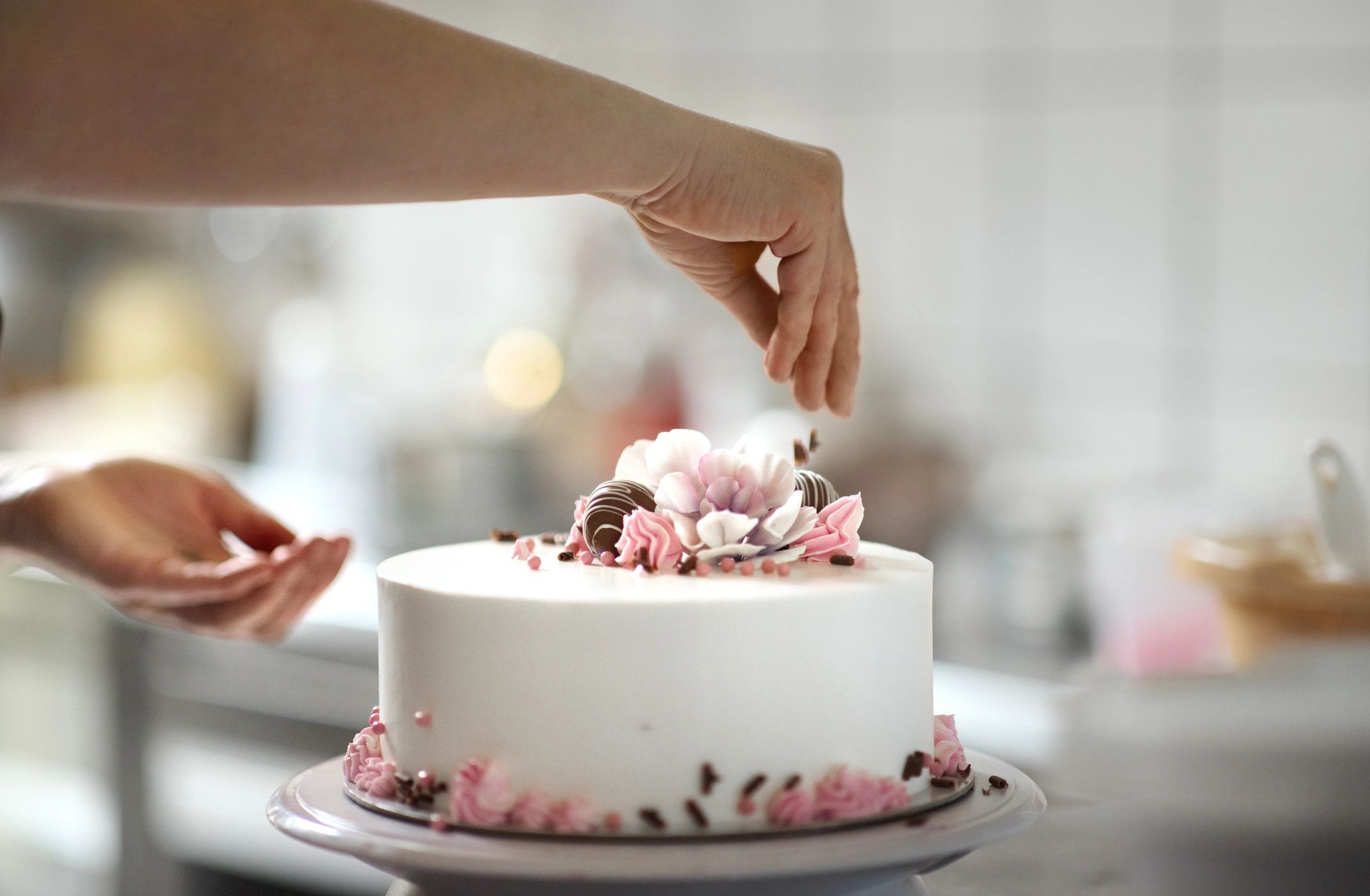 Hands decorating a cake with frosting at a bakery